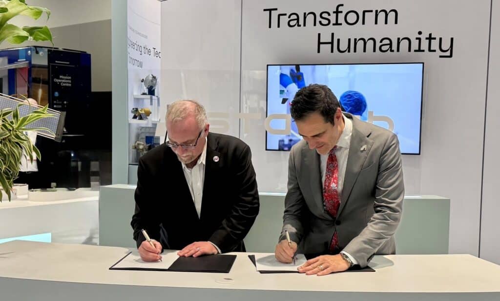 Two men signing documents at corporate event.